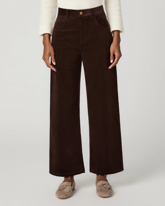 A model is wearing dark brown wide-leg corduroy pants, styled with a cream knit sweater and taupe tassel loafers, against a light gray studio background.