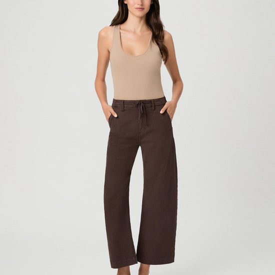 A woman modeling a beige ribbed tank top and dark brown wide-leg cropped pants with a drawstring waist, paired with brown slide sandals, against a light gray studio background.