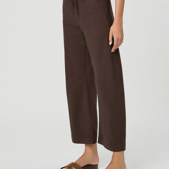 A model wearing dark brown wide-leg cropped pants with a drawstring waistband, paired with brown slide sandals, against a light gray studio background.