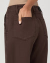 Close-up of a person wearing dark brown wide-leg pants, showing the back pocket and hand in the pocket, against a light gray background.