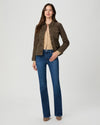 A woman modeling a dark brown utility jacket over a beige top and blue jeans, standing against a light gray studio background.