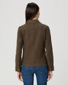 A woman viewed from the back wearing an olive brown utility jacket and blue jeans against a light gray studio background.
