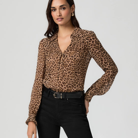 Woman wearing a leopard print blouse froM PAIGE and black pants on a light gray background