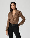 Woman wearing a leopard print blouse froM PAIGE and black pants on a light gray background