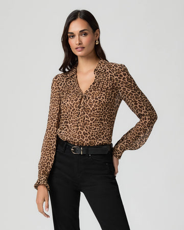 Woman wearing a leopard print blouse froM PAIGE and black pants on a light gray background