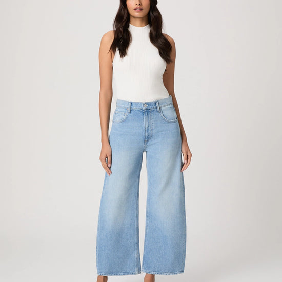 Woman wearing light blue jeans and a white top on a plain background from Paige