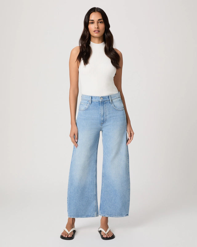 Woman wearing light blue jeans and a white top on a plain background from Paige