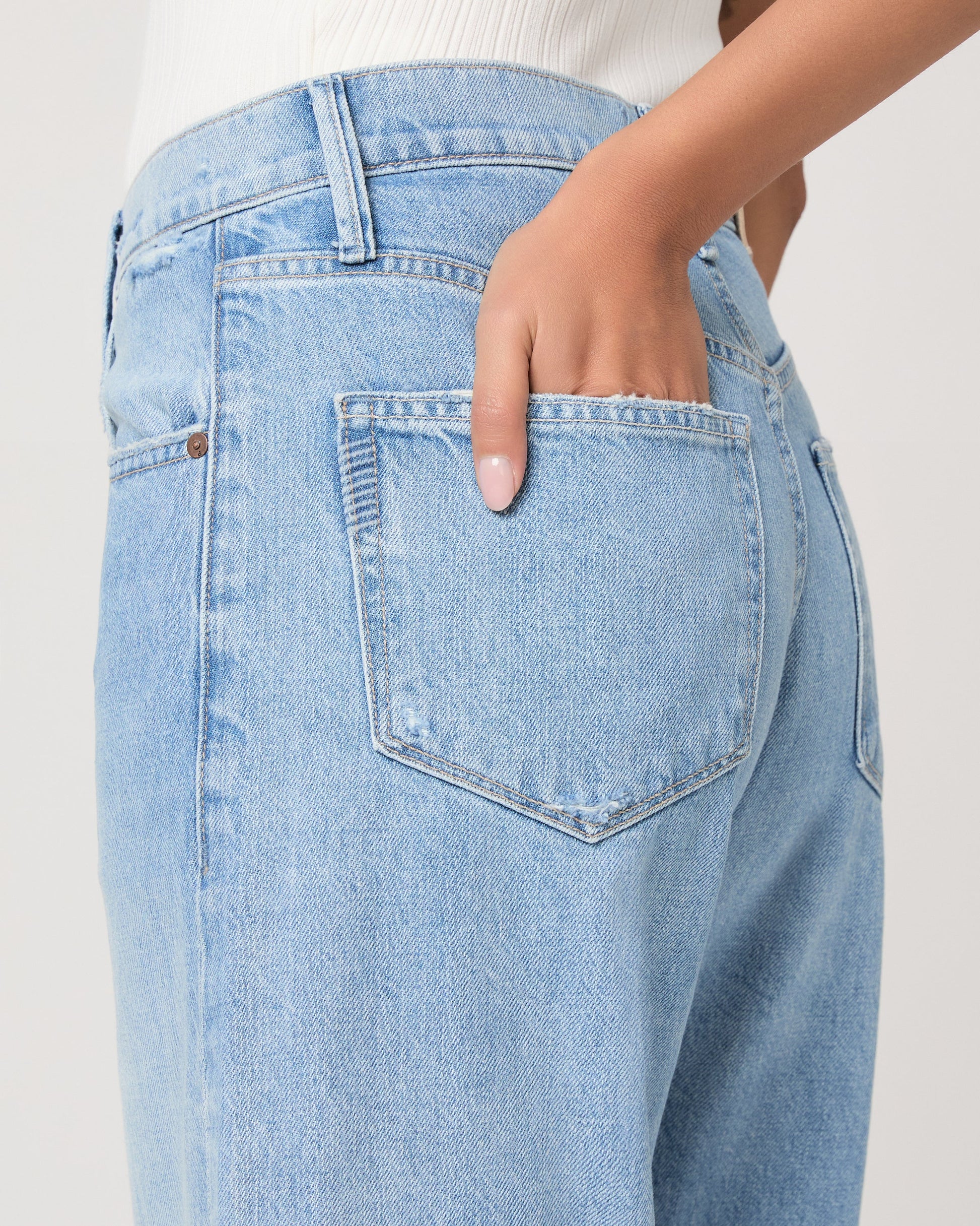 Light blue jeans with a brand logo on a plain background from Paige