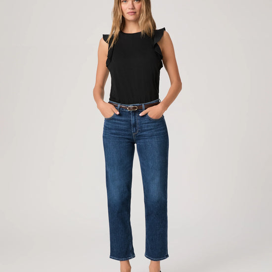 Woman wearing a black top and blue jeans By Paige on a white background