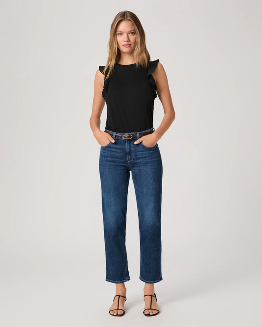 Woman wearing a black top and blue jeans By Paige on a white background