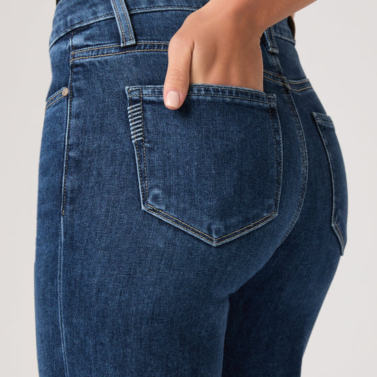 Person wearing blue jeans by paige on a plain background close up