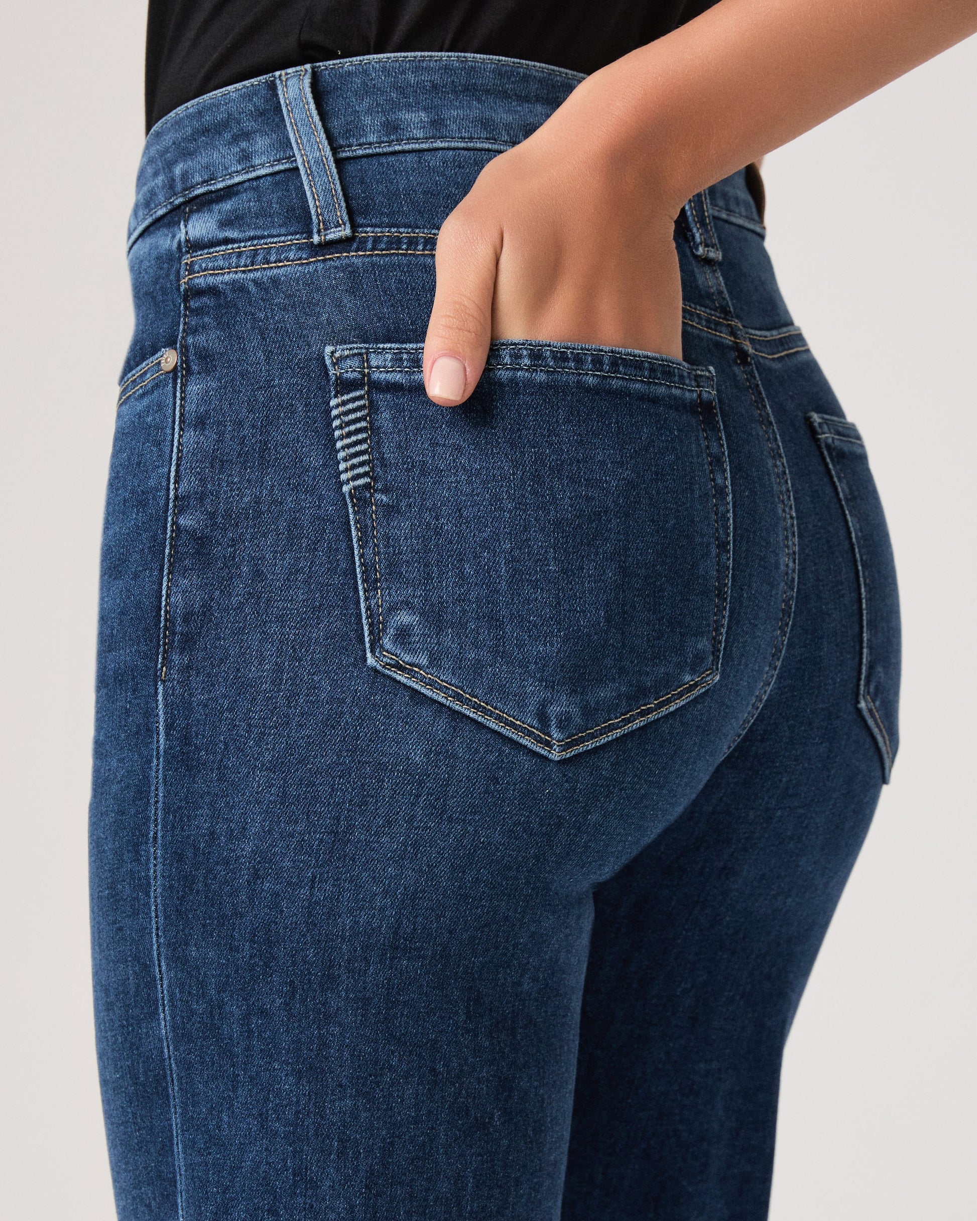 Person wearing blue jeans by paige on a plain background close up
