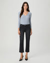 A woman modeling a light blue ribbed knit long-sleeve top with decorative buttons down the front, paired with dark cropped jeans and black heels, against a light gray studio background.