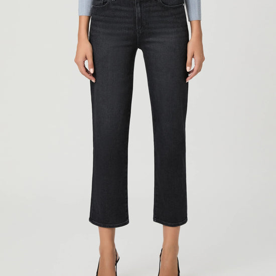 A model wearing a pair of dark charcoal gray cropped jeans, styled with a light blue ribbed long-sleeve top and black pointed-toe heels, against a light gray studio background.