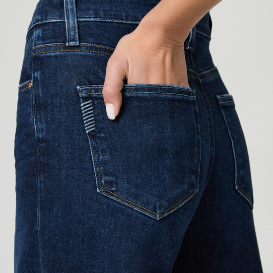 Close-up of a person wearing dark blue jeans with a neutral background