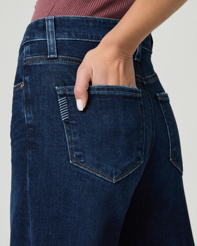 Close-up of a person wearing dark blue jeans with a neutral background