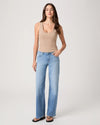 Woman wearing a beige tank top and light blue jeans from Paige on a white background