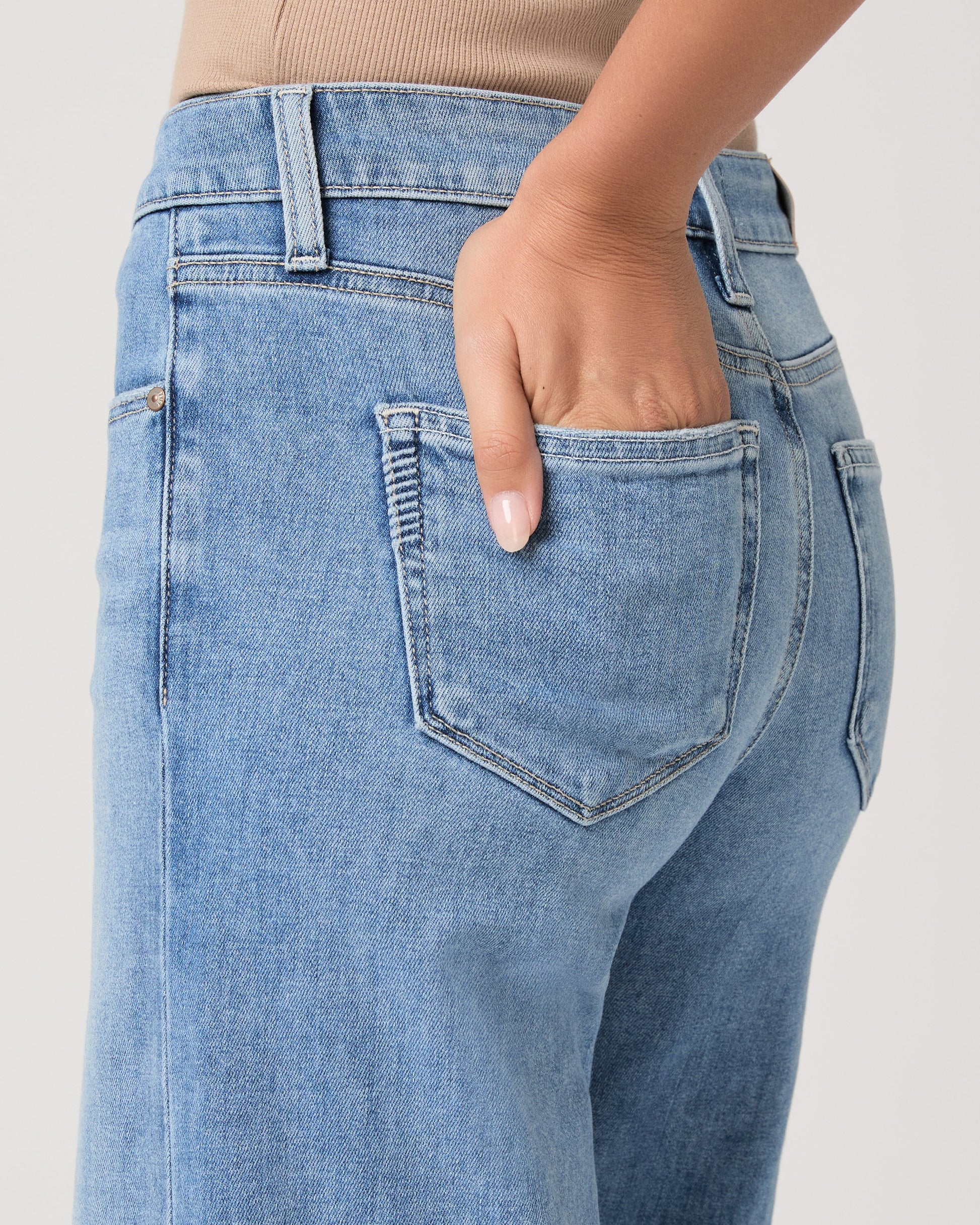 Woman wearing light blue jeans from Paige on a white background close up of pocket
