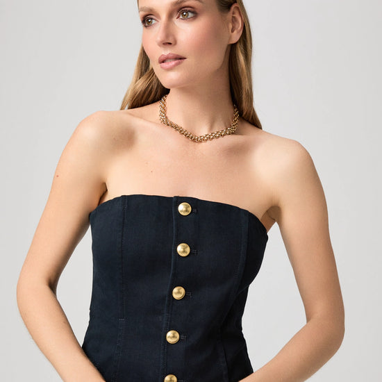 Woman wearing a strapless denim top with gold buttons and a gold necklace on a light gray background from Paige