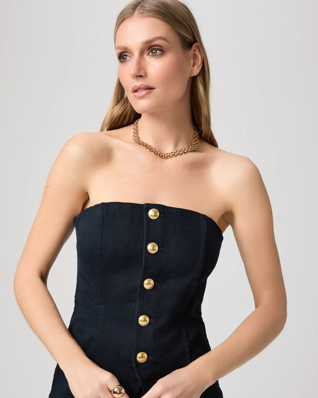 Woman wearing a strapless denim top with gold buttons and a gold necklace on a light gray background from Paige