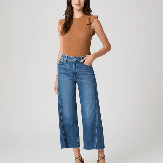 Woman wearing paige blue jeans and a brown top on a white background