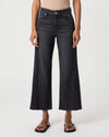 A model wearing a pair of dark charcoal gray wide-leg cropped jeans with a raw hem, paired with black slide sandals, shown against a plain light gray studio background.