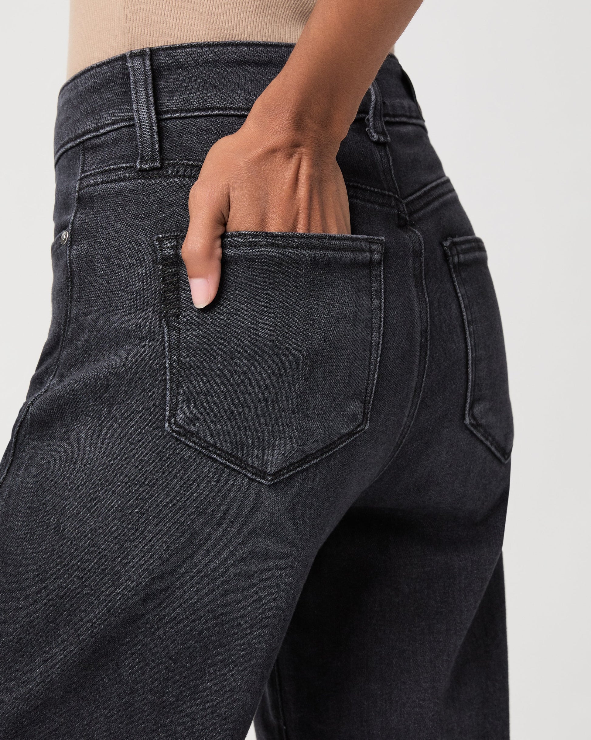 Close-up of a person wearing dark charcoal gray jeans, showing the back pocket and hand in the pocket.