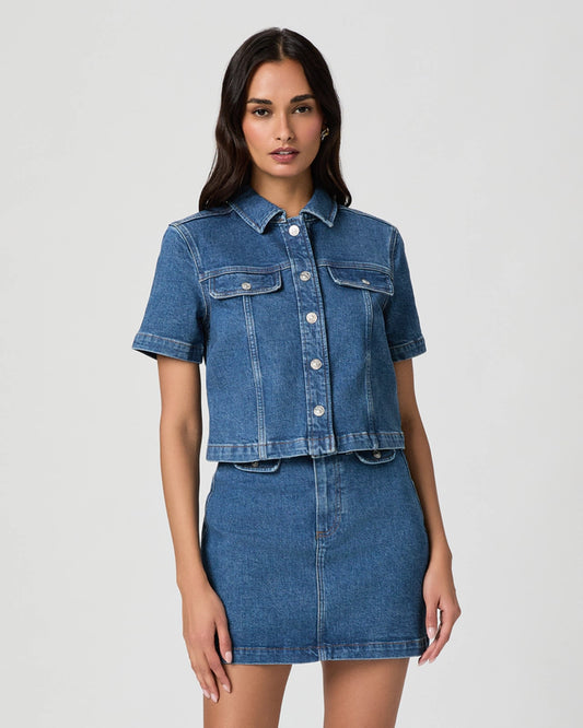 Woman wearing a blue denim jacket and skirt on a light gray background