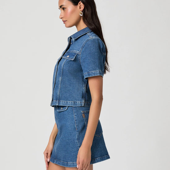 Woman wearing a blue denim jacket and skirt set on a light gray background