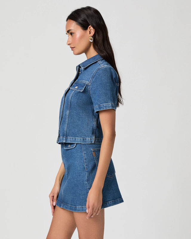 Woman wearing a blue denim jacket and skirt set on a light gray background