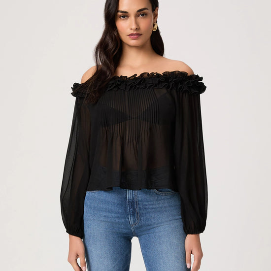 Woman wearing a black off-shoulder top and blue jeans on a light gray background