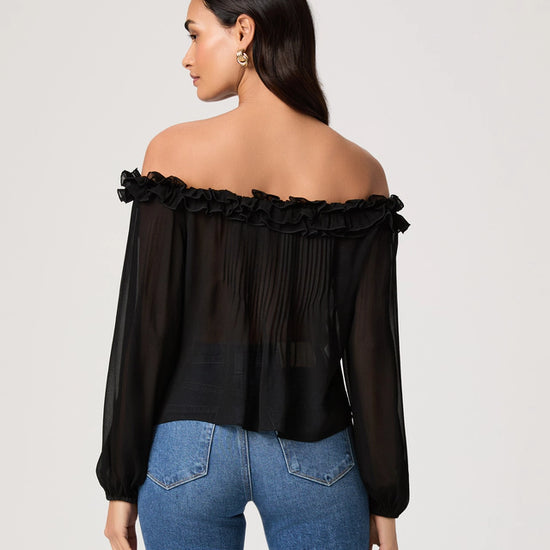 Woman wearing a black off-shoulder top and blue jeans on a plain background