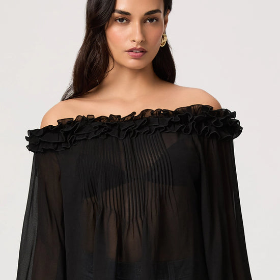 Woman wearing a black off-shoulder top with ruffled details on a white background