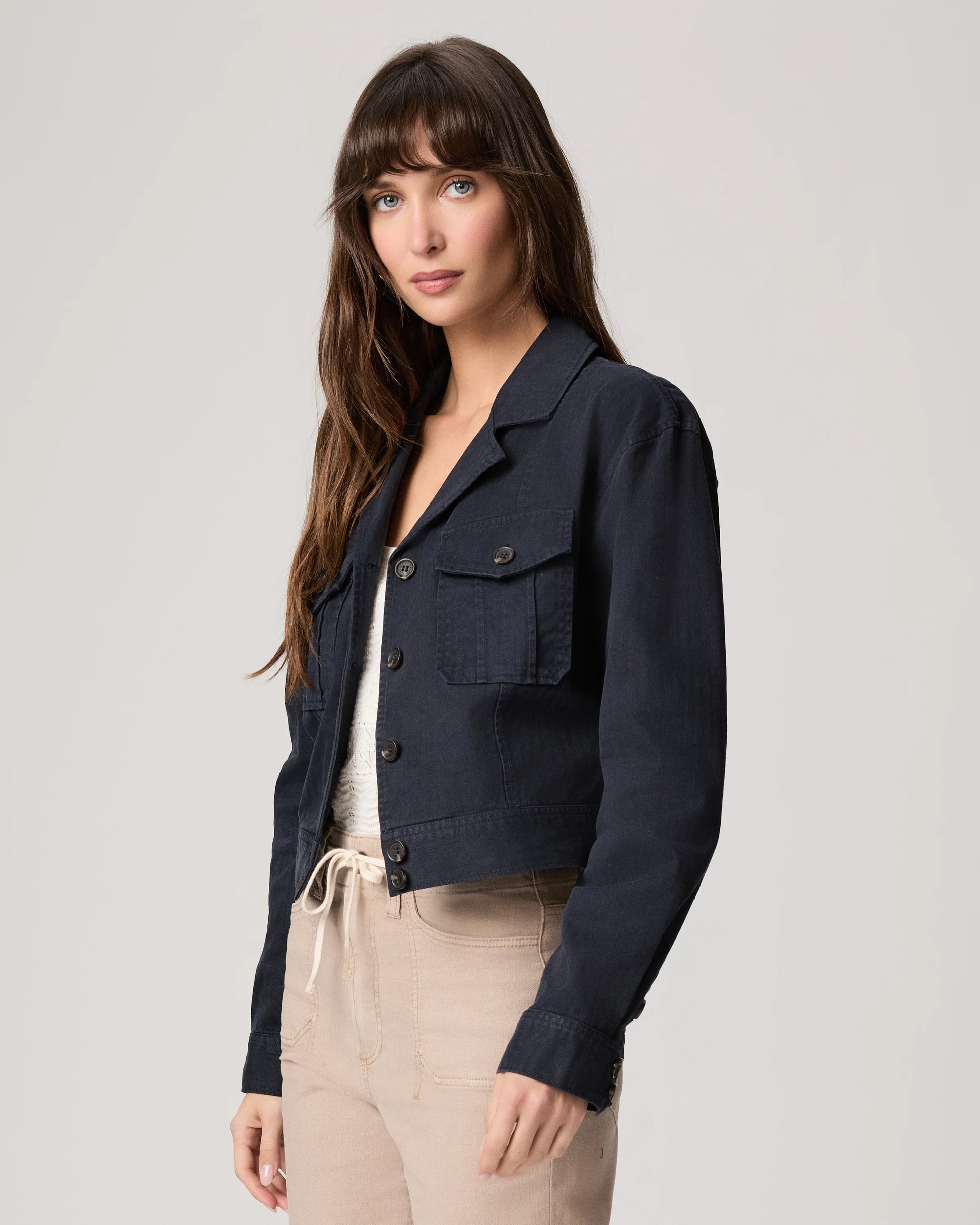 Woman wearing a navy jacket over a white top and beige pants on a light gray background