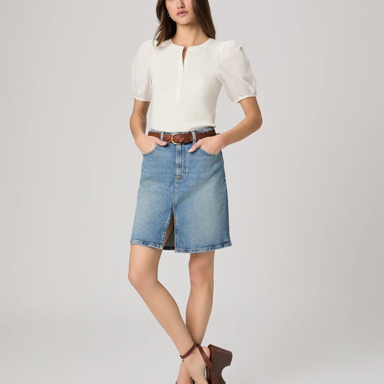 Woman wearing a white blouse and denim skirt on a plain background