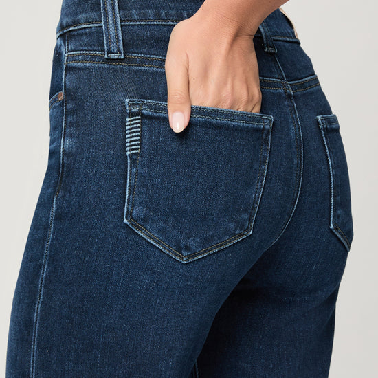 Close-up of blue jeans with a hand in the pocket against a neutral background