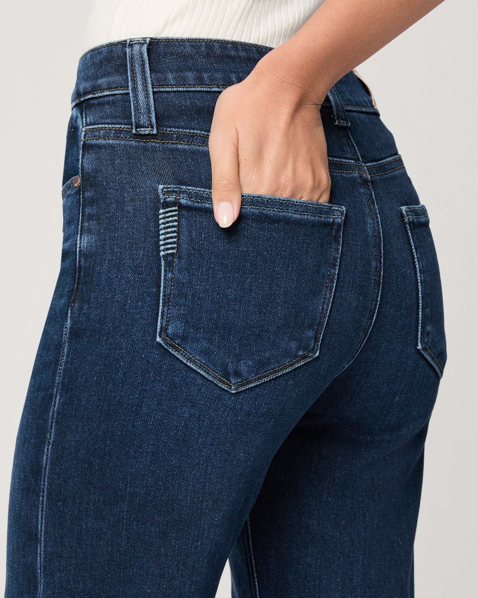 Close-up of blue jeans with a hand in the pocket against a neutral background