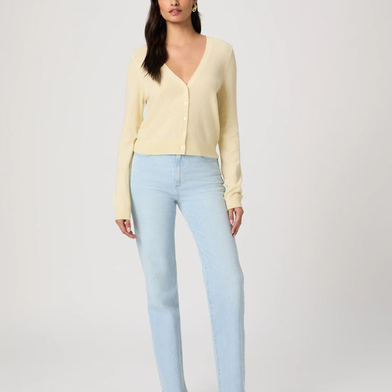 Woman wearing a light yellow cardigan by Paige and light blue jeans on a white background
