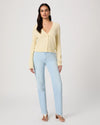 Woman wearing a light yellow cardigan by Paige and light blue jeans on a white background