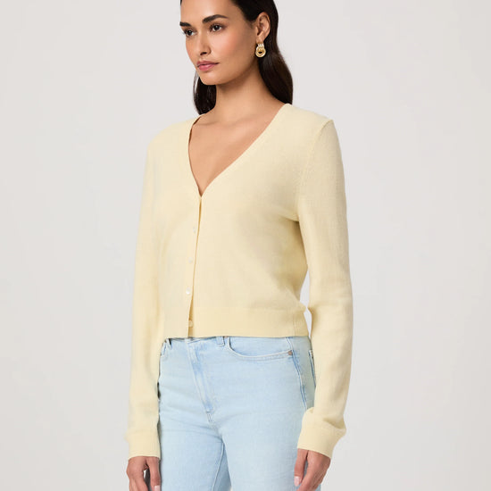 Woman wearing a light yellow cardigan by Paige and light blue jeans on a white background side view