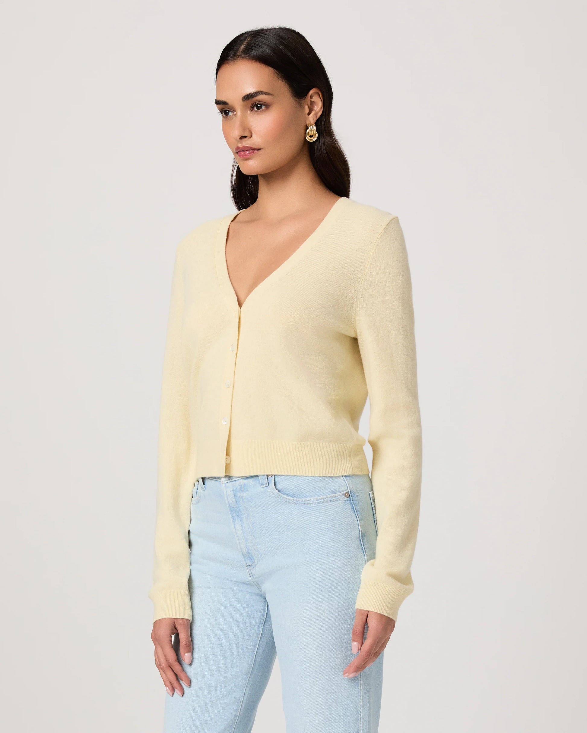 Woman wearing a light yellow cardigan by Paige and light blue jeans on a white background side view