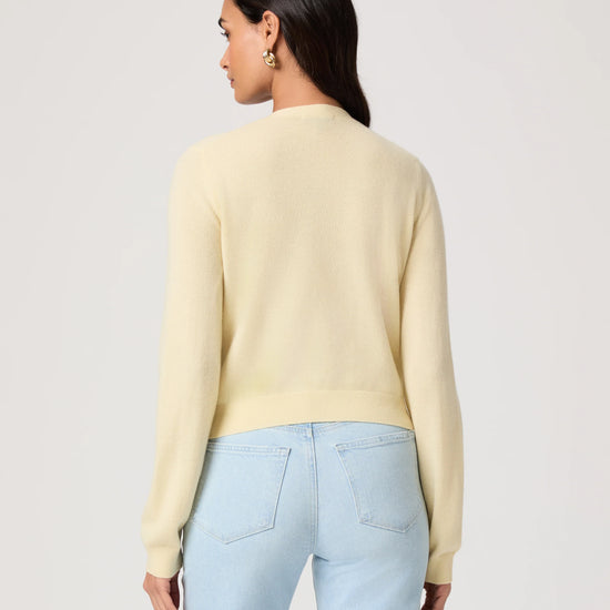 Woman wearing a light yellow cardigan by Paige and light blue jeans on a white background rear view
