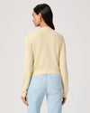 Woman wearing a light yellow cardigan by Paige and light blue jeans on a white background rear view