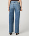 Rear view of a model wearing high-waisted, wide-leg blue denim jeans with a light tan leather patch on the back waistband, paired with black heels against a light gray studio background.