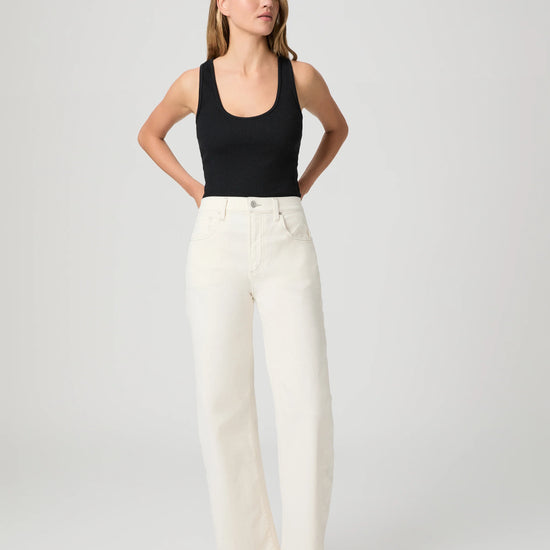 Woman wearing a black tank top and white Paige Jeans on a plain background