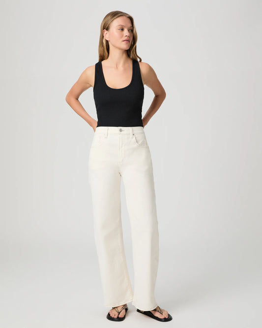 Woman wearing a black tank top and white Paige Jeans on a plain background