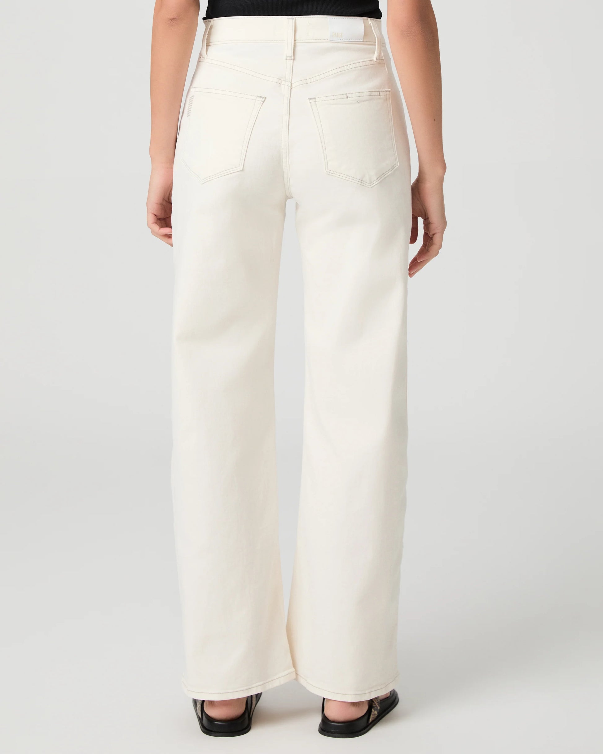Person wearing white Paige jeans on a plain background rear view