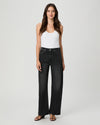 A woman modeling a pair of high-waisted, wide-leg black denim jeans with a white tank top and black sandals, standing against a light gray studio background.