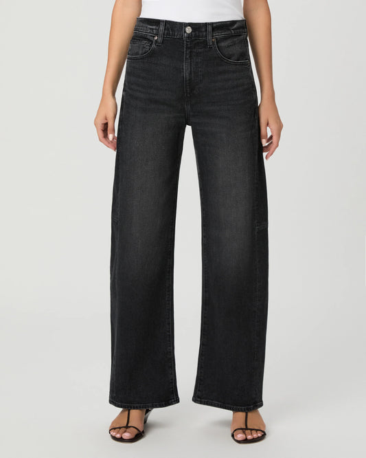 A model wearing a pair of black wide-leg denim jeans with a white top and black sandals, shown from the waist down against a light gray studio background.