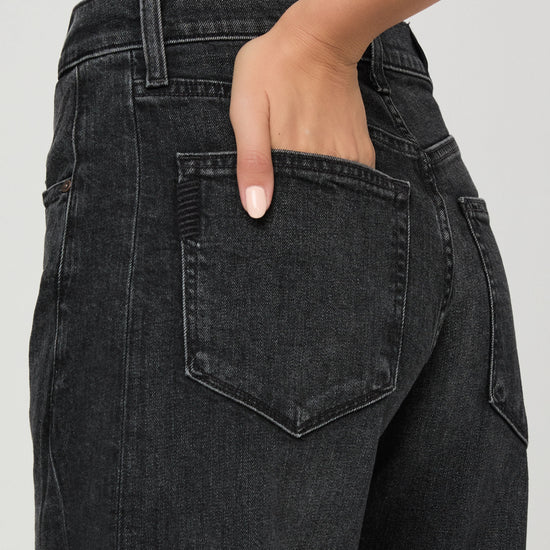 Close-up of a person wearing dark charcoal gray denim jeans, showing the back pocket and hand in the pocket.